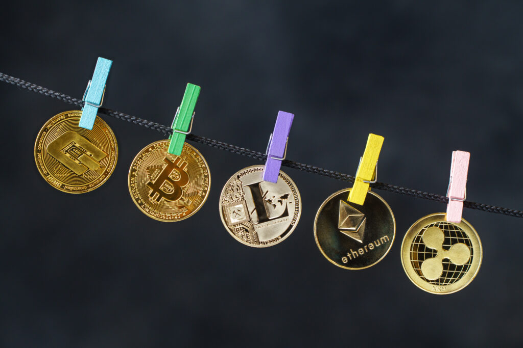 Five gold coins with different crypto logos embossed on them hanging on a rope, clipped by wooden clothespins of various colours.