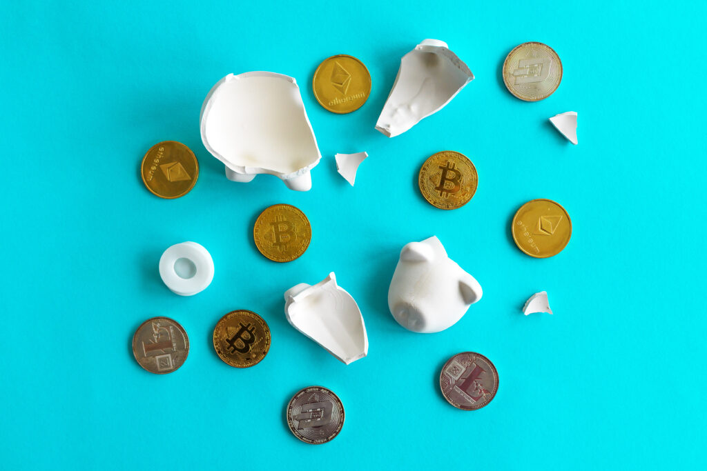 A broken piggy bank with cryptocurrency tokens on a blue surface.