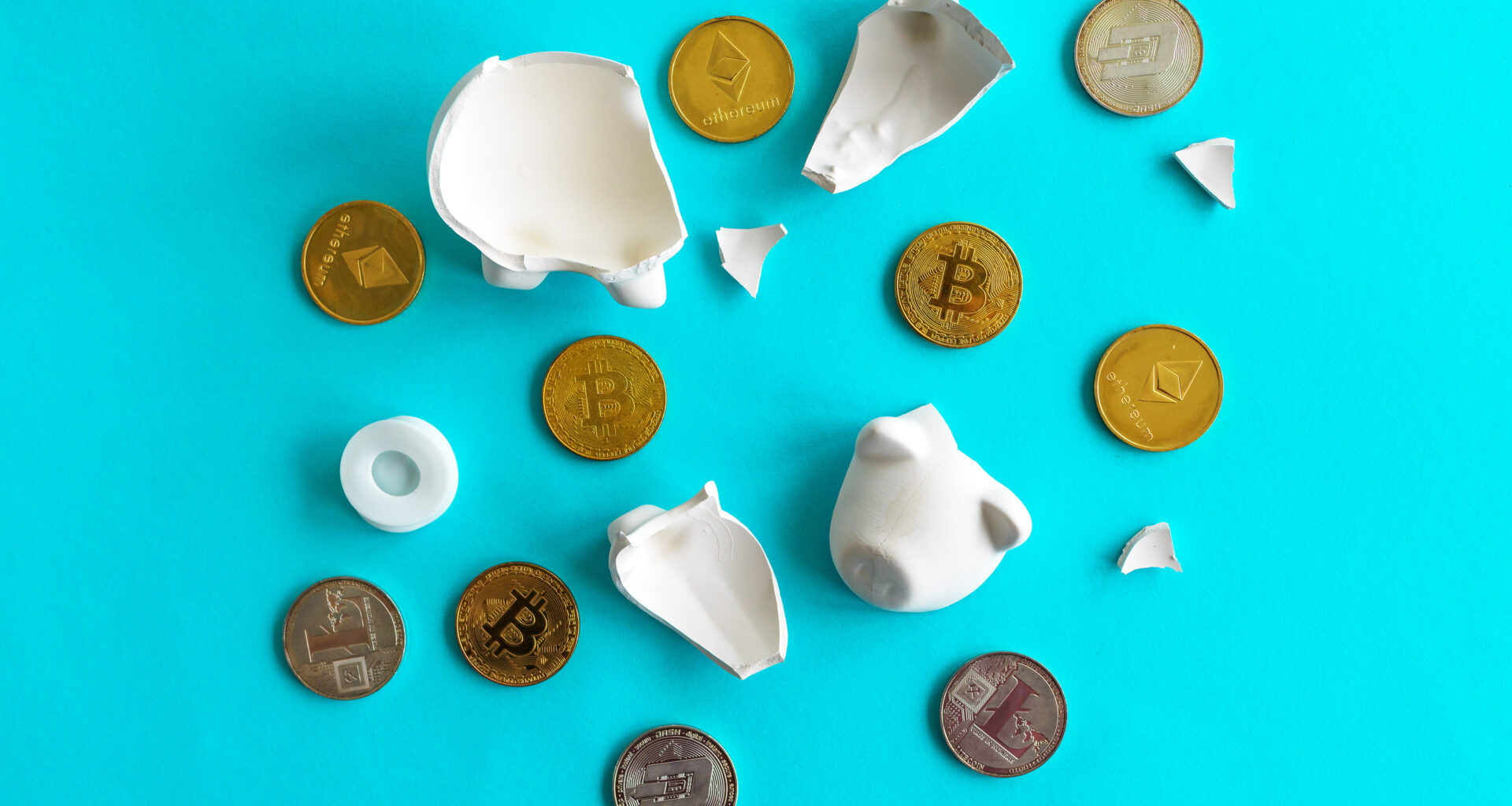 A broken piggy bank with cryptocurrency tokens on a blue surface.