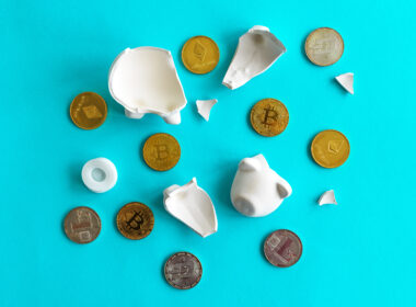 A broken piggy bank with cryptocurrency tokens on a blue surface.