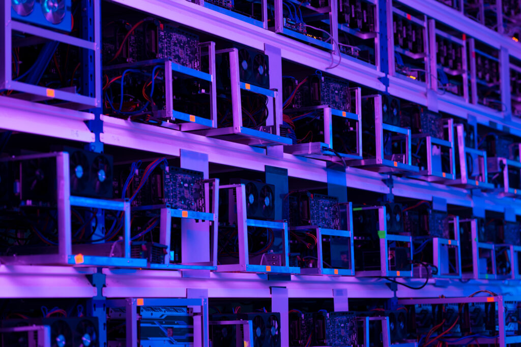 Many computer mining units are lined up on shelves washed in purple light.