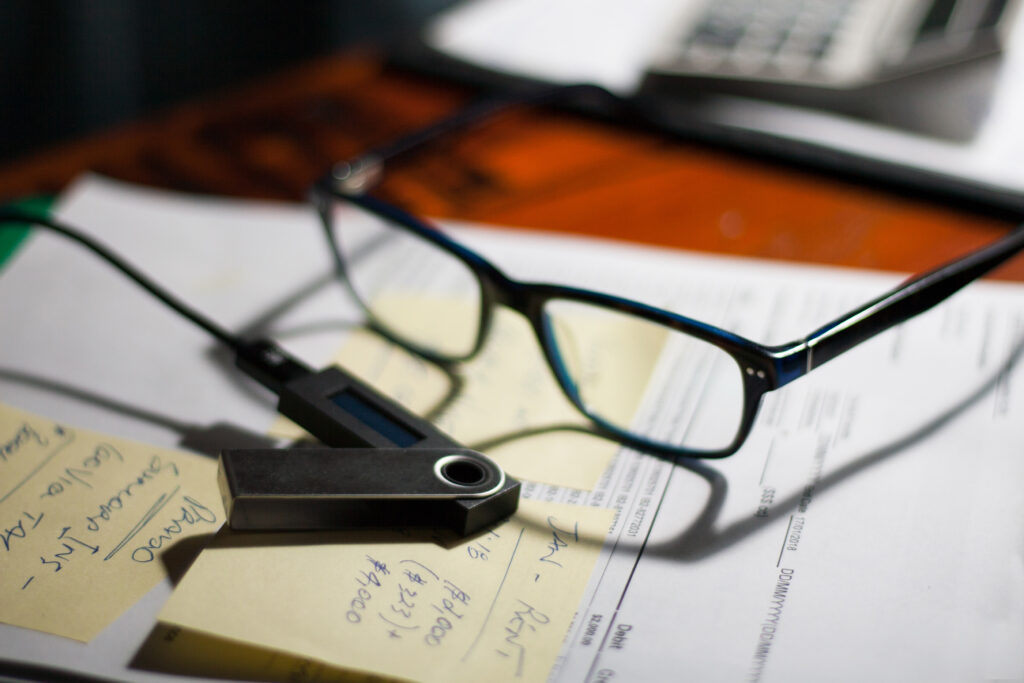 Glasses and Ledger Nano wallet on a folder with documents, bills and notes on a desk