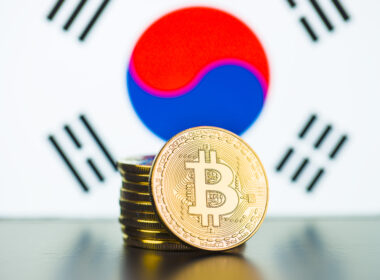 A stack of golden coins with the bitcoin logo embossed on it, in front of the South Korean flag.