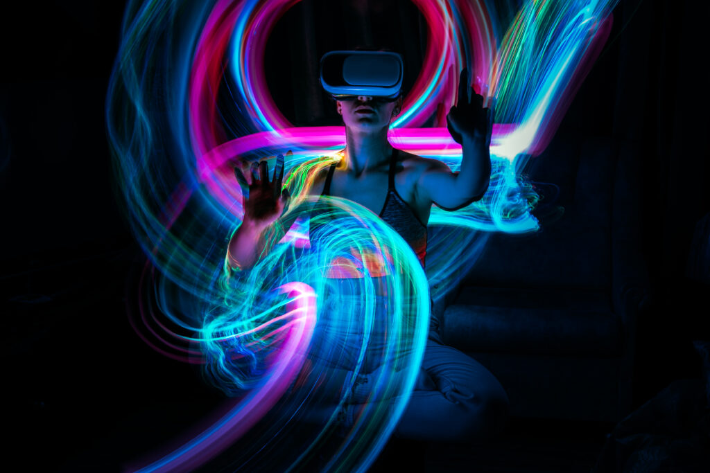 A woman wearing a VR headset is in a dynamic pose in a dark room. Digitally imposed colourful streaks of light surround her.