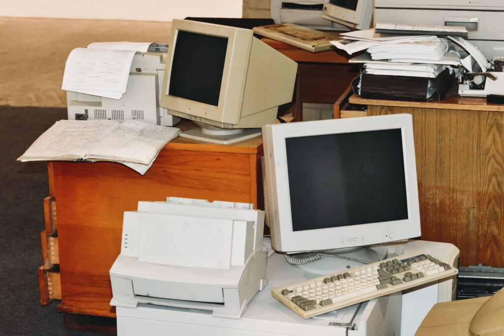 Old computers, printers, typewriters, keyboards ready to trash from office. Retro device, screens and monitors on table and floor