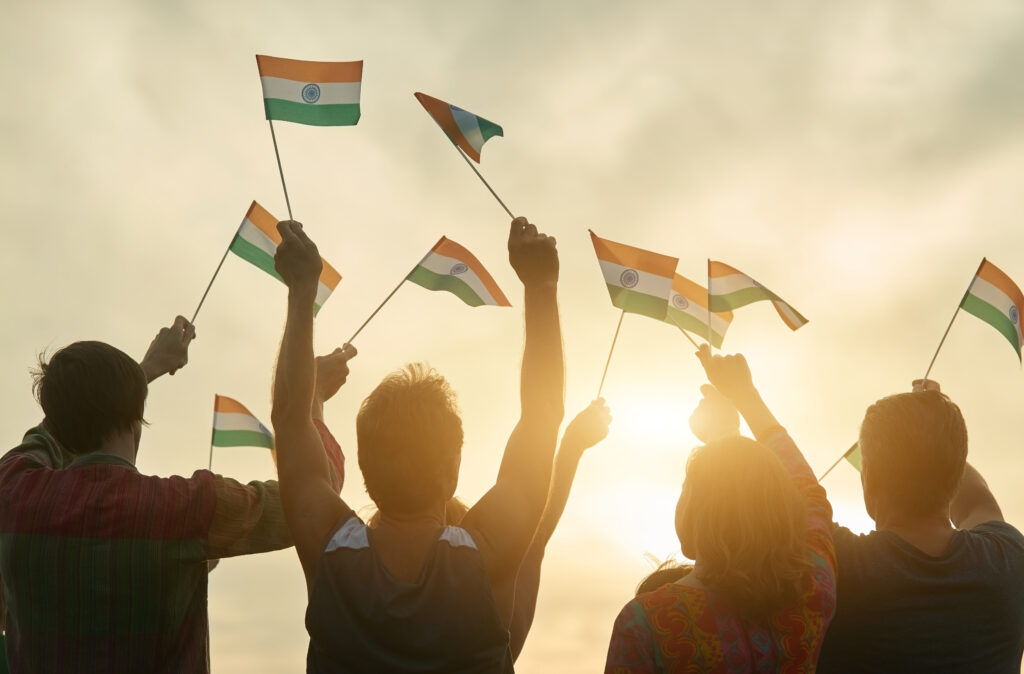 Five people holding up flags of India. Only their silhouette is visible against a golden sunset sky.