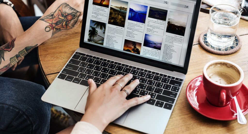 A person browsing the web on a laptop. A small red cup of coffee on the right.