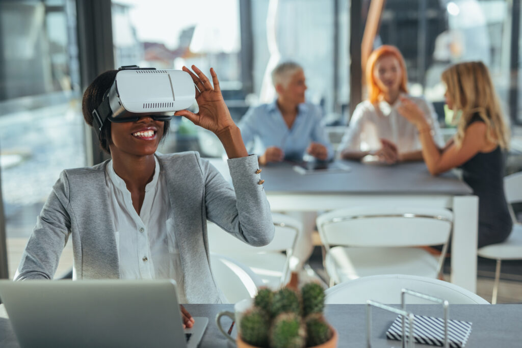 Young businesswoman holding a virtual reality headset, her colleagues sitting in the background.