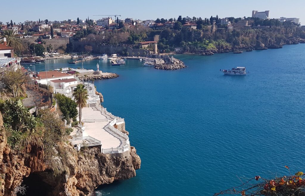 Antalya in Turkey. There is a cliff on the left side and blue seas on the right side of the photo. A small yacht is in the middle of the sea.
