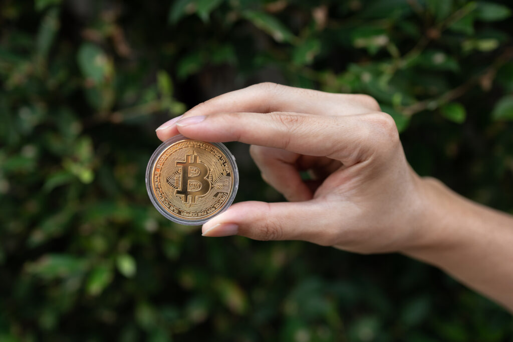 Young man holding BTC Bitcoin in hand with green bush in background