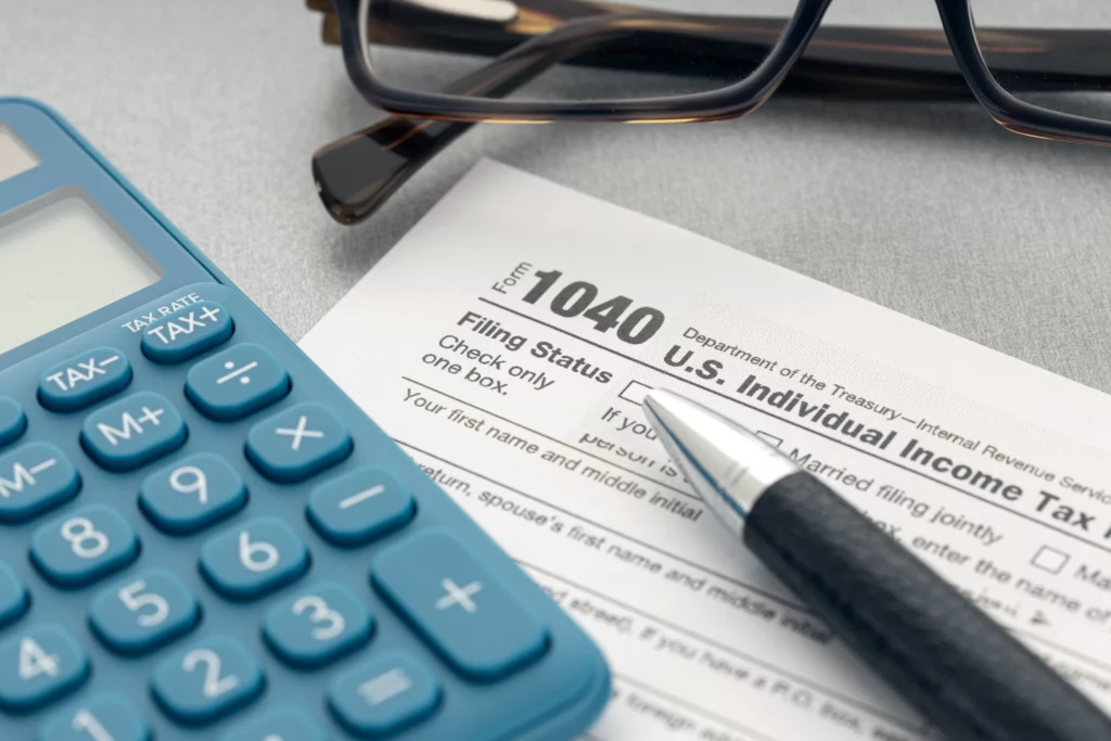 a blue calculator sits on a table on the left, on top of a tax sheet and a pen