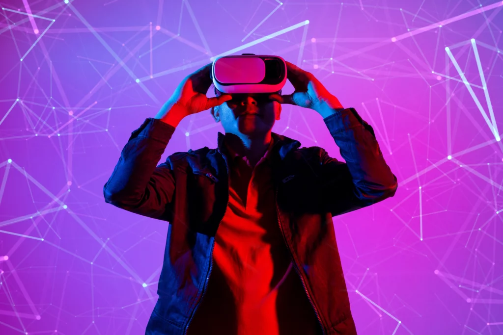a man is wearing a VR headset and is holding it with both hands. He is doused in red light and is standing before a purple background with digital-looking lines across it.