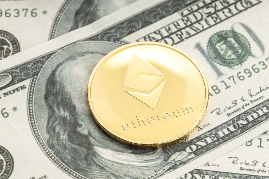 A gold Ethereum coin on top of a dollar bill, covering its face.