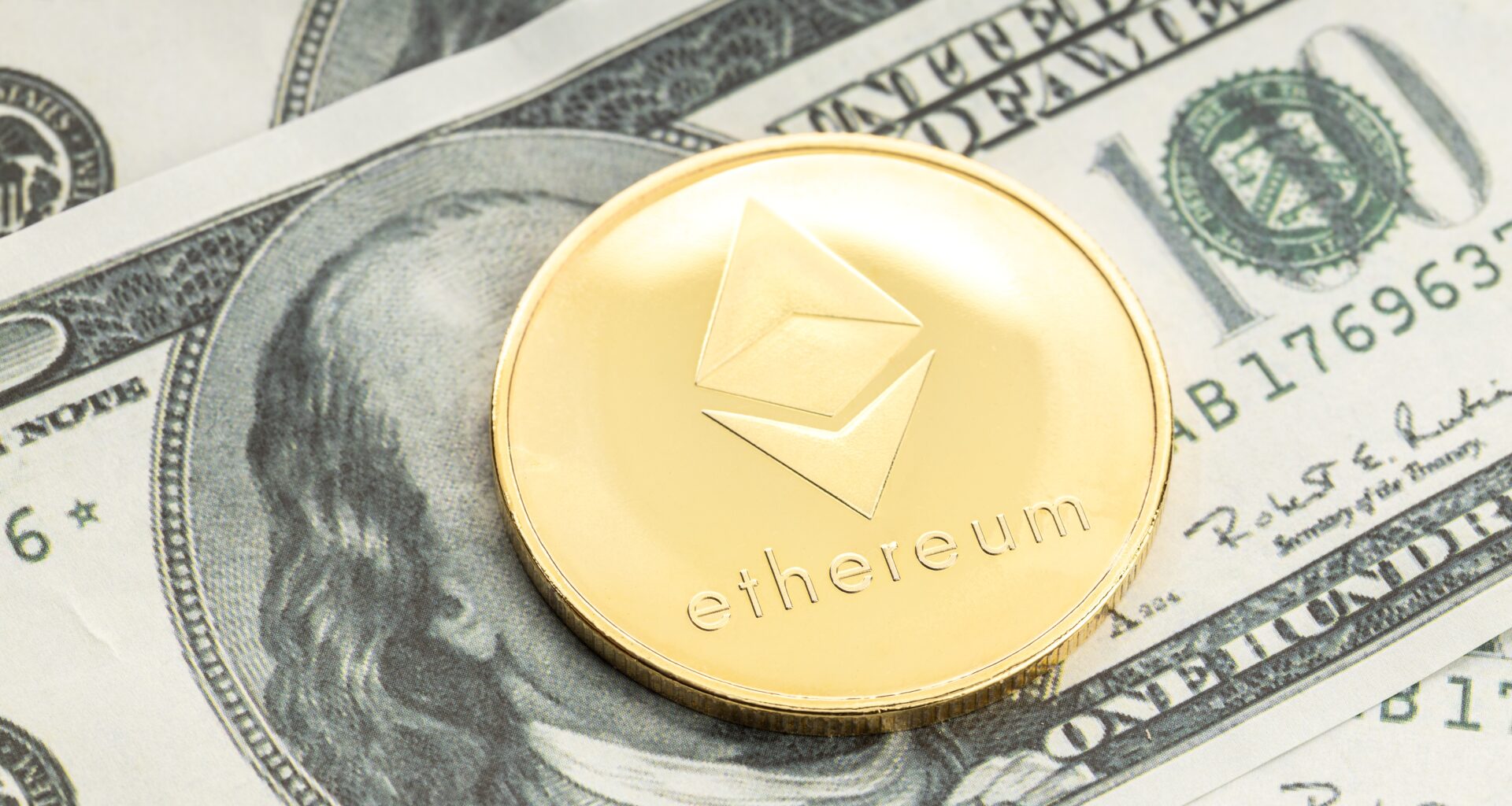 A gold Ethereum coin on top of a dollar bill, covering its face.