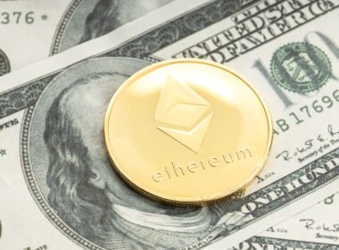 A gold Ethereum coin on top of a dollar bill, covering its face.