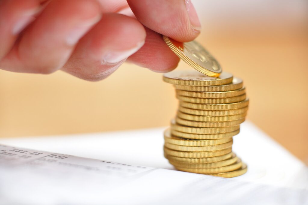 Someone is placing a gold coin on top of a stack of gold coins.