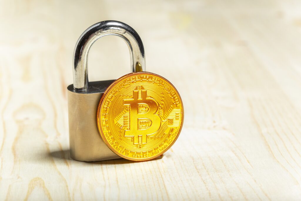 A gold Bitcoin is in front of a lock padlock.