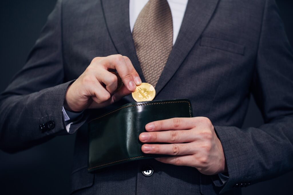 A man in a business suit is holding a wallet and a gold Bitcoin.
