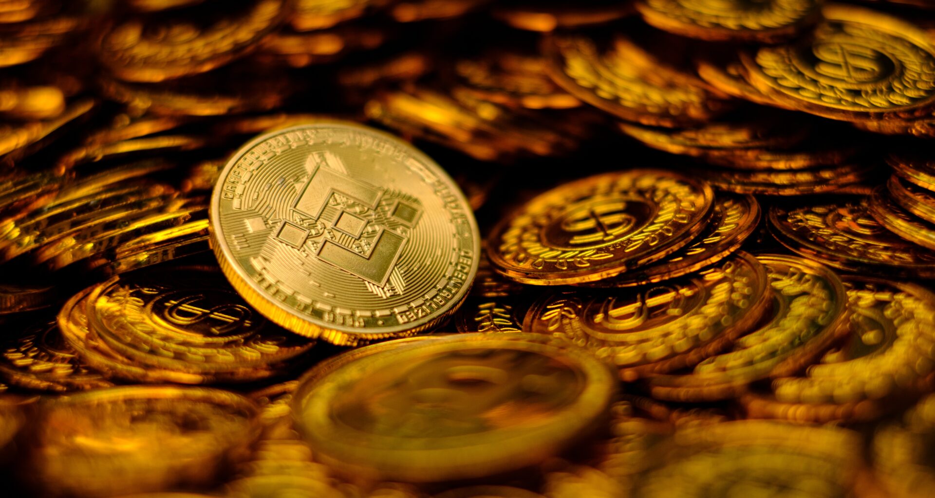 A gold Binance coin sits on top of a pile of other gold coins.