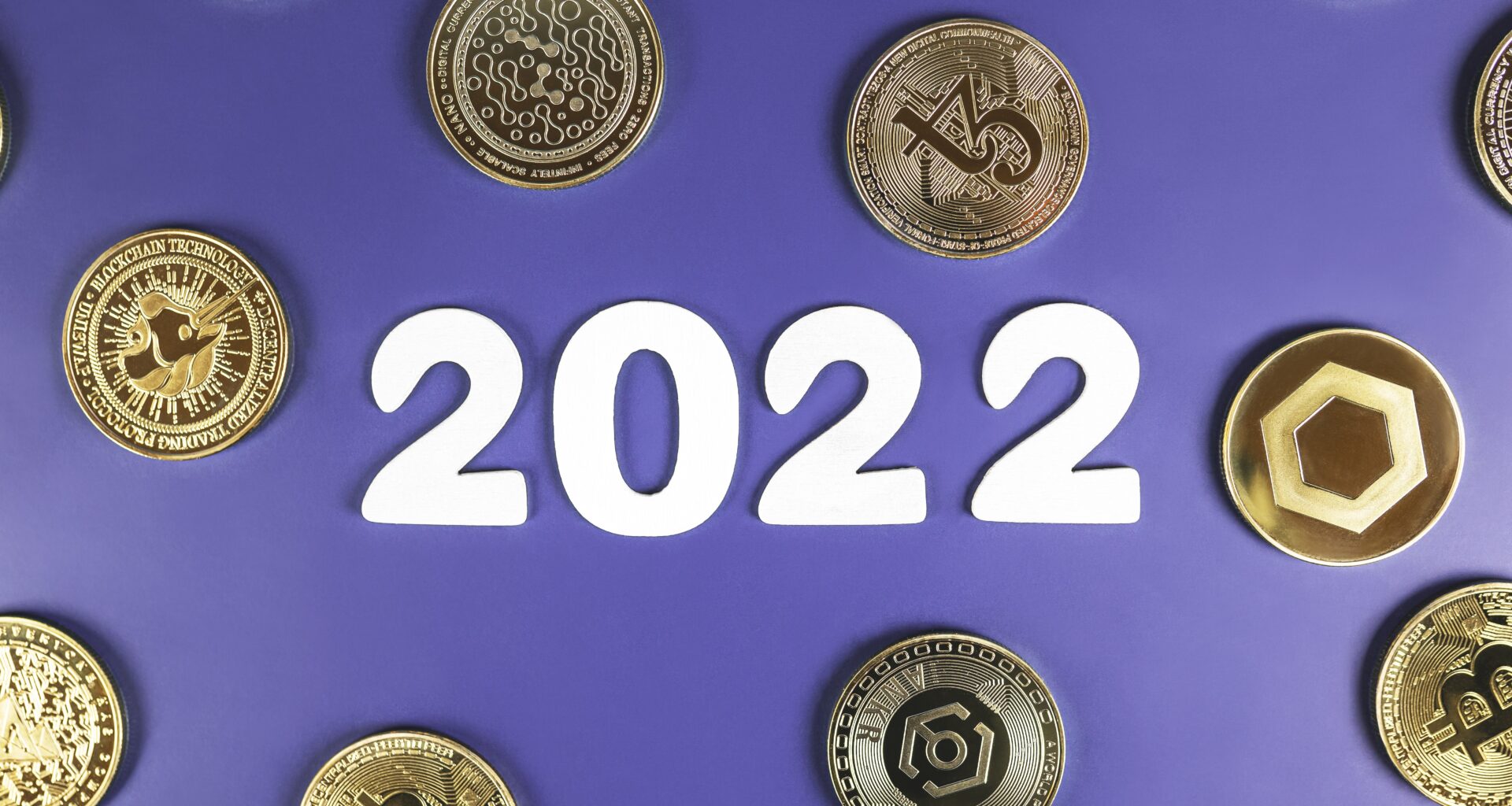 The number "2022" in white against a purple background. There are several gold coins with different crypto logos embossed on them scattered around the background.