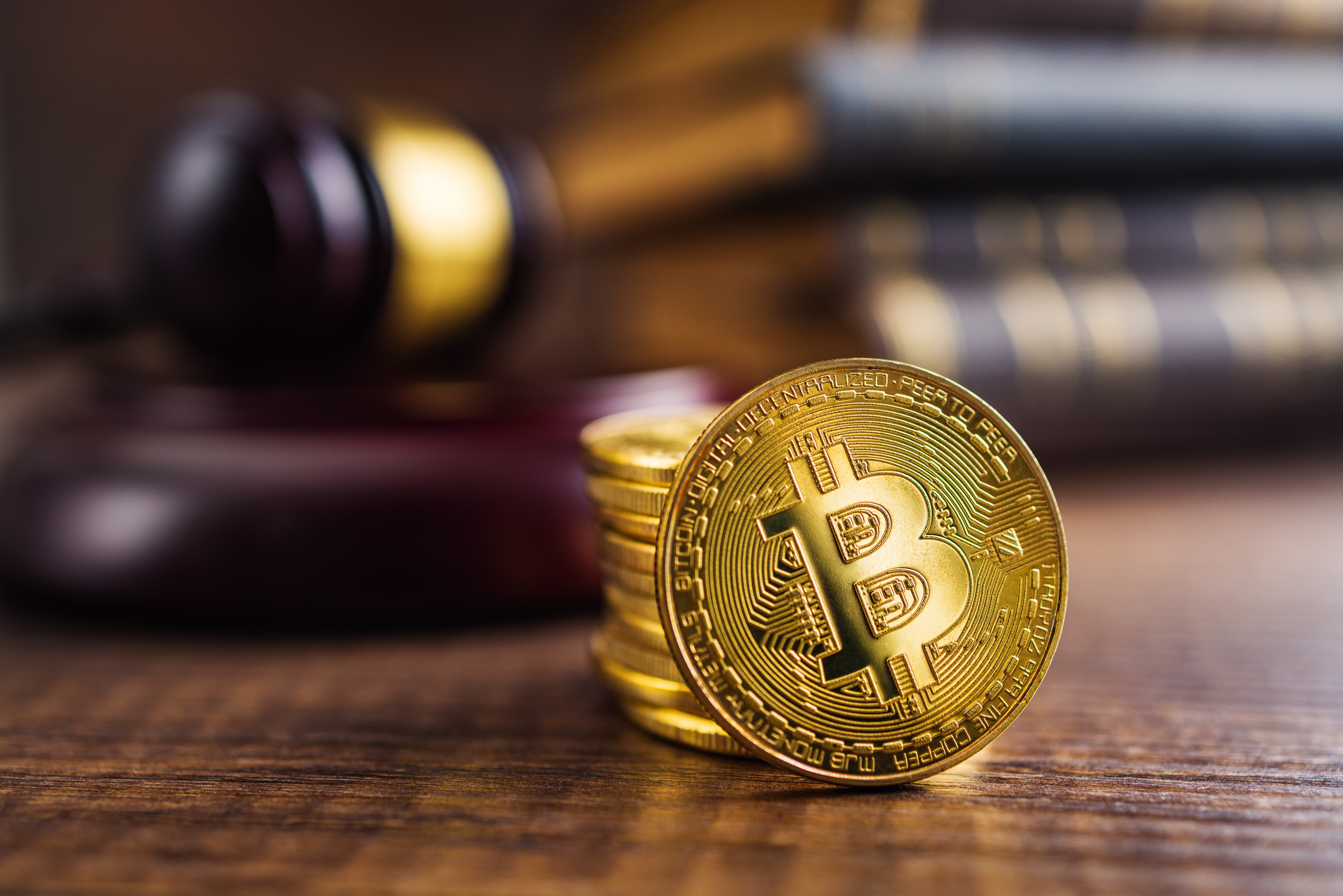 A stack of gold Bitcoins sit on a wooden table in front of a gavel.